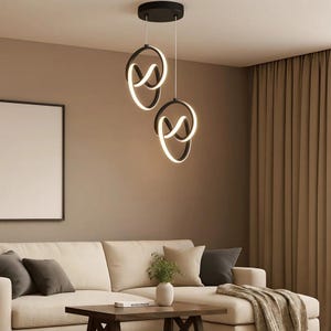 Könnte beinhalten: Zwei moderne Pendelleuchten mit schwarzem Rahmen und weißem, geschwungenem Lichtdesign. Die Leuchten hängen an einer schwarzen Deckenleuchte. Sie hängen über einem cremefarbenen Sofa in einem Wohnzimmer.