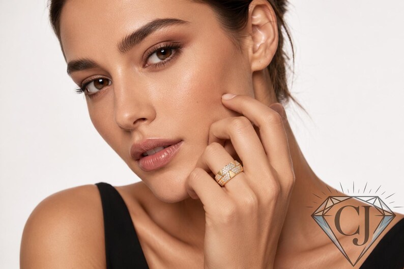 May include: A woman's hand displaying two gold rings, each adorned with small, glittering stones. The rings are on the ring finger. The woman wears a black top and has natural makeup.