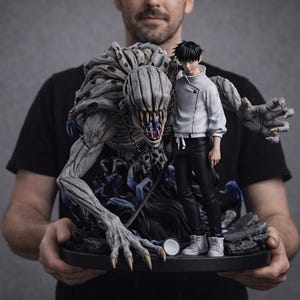 May include: A detailed statue featuring a character in a white jacket and black pants, standing next to a large, monstrous creature with sharp teeth and claws. The statue is predominantly gray and blue, set on a black base.