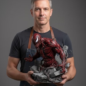 Puede incluir: Estatua detallada en rojo y negro de un personaje de cómic, emergiendo de una base de piedra. La figura tiene una expresión amenazante y la sostiene una persona con un delantal de mezclilla.