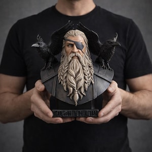 May include: A detailed bust of a bearded man with an eye patch, flanked by two black ravens. The bust has a long, flowing white beard and is set on a dark base. The bust is held by a person wearing a black shirt.