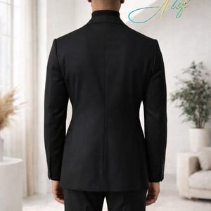 May include: A black suit, viewed from the back, with a matching blazer and trousers. The suit is tailored and has a classic design. The person is wearing a black turtleneck. The background is a bright, modern interior.