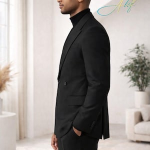 May include: A black double-breasted suit with a black turtleneck. The suit has a classic design with a notched lapel and a two-button closure. The person is standing in a well-lit room with a neutral background. The image includes the signature "Alif".