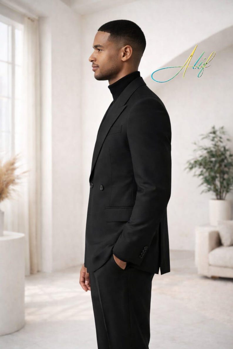 May include: A black double-breasted suit with a black turtleneck. The suit has a classic design with a notched lapel and a two-button closure. The person is standing in a well-lit room with a neutral background. The image includes the signature "Alif".