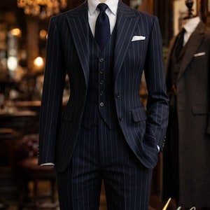 Pu&ograve; includere: Un completo gessato blu navy esposto su un manichino. L'abito include giacca, gilet e pantaloni, abbinati a una camicia bianca e cravatta blu navy. Un fazzoletto bianco &egrave; nel taschino della giacca.