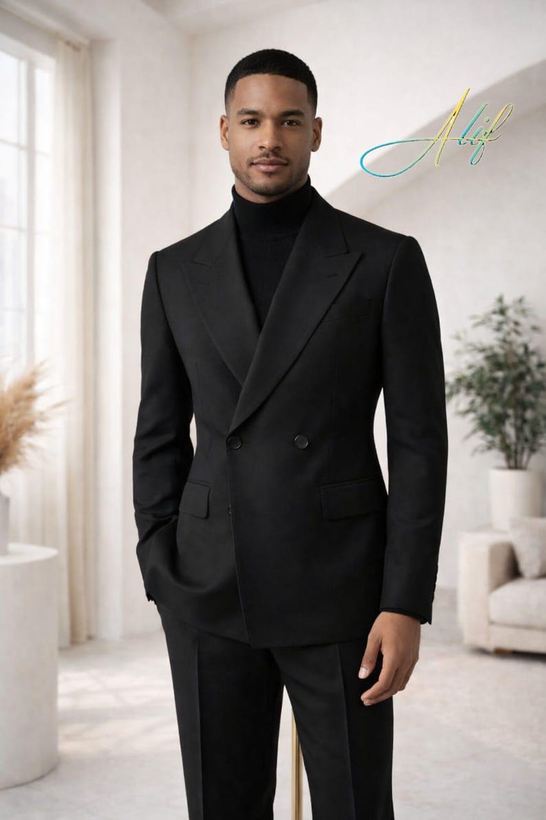May include: A black double-breasted suit with a black turtleneck. The suit has a classic design with a notched lapel and two buttons. The person is standing in a well-lit room with a neutral background.