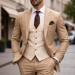 May include: A smart three-piece suit in a tan colour, featuring a matching waistcoat, white shirt, and brown tie. The suit includes a pocket square and a gold wristwatch. A classic formal outfit for men.