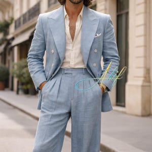 Può includere: Un abito azzurro a doppio petto con pantaloni a gamba larga. L'abito è abbinato a una camicia con bottoni color crema. La persona indossa occhiali da sole e un orologio d'oro. L'abito sembra essere realizzato in lino o tessuto leggero simile.