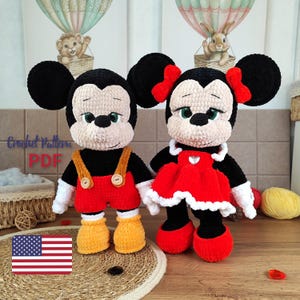 Puede incluir: Dos muñecos de ganchillo, uno masculino y otro femenino, que se asemejan a personajes de dibujos animados. El muñeco masculino lleva pantalones cortos rojos con tirantes y zapatos amarillos. La muñeca femenina lleva un vestido rojo con cuello blanco y zapatos rojos.