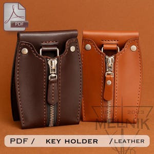 May include: Two leather key holders are shown, one in dark brown and the other in tan. Each has a zip closure and metal hardware. The key holders are rectangular with rounded edges and a loop at the top. The image includes the text "PDF / KEY HOLDER / LEATHER".