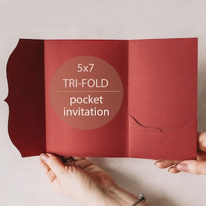 Può includere: Un invito tascabile a tre ante di colore rosso intenso, tenuto aperto per mostrare l'interno. L'invito presenta un bordo decorativo sul lato sinistro e una tasca sul lato destro. Il testo sul fronte recita "5x7 TRI-FOLD pocket invitation."