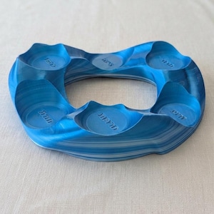 May include: A blue, ring-shaped object with six circular indentations. The object has a marbled appearance with light and dark blue stripes. Each indentation has the word "JETT" printed on it. The object is likely a coaster or a similar item.
