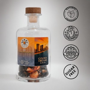 May include: A clear glass bottle with a wooden stopper, filled with dark ingredients. The label reads "Golden Dreams by the Sea" and "Sunny Isles Beach." Additional labels indicate the product is natural, handmade, premium, and sugar-free.