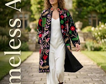 May include: A black long-sleeve coat featuring vibrant, multi-colored floral and leaf embroidery, worn over a simple white midi dress with brown leather boots. The text "Timeless Art" is printed vertically in white on the left side of the image.