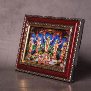 May include: A framed religious artwork featuring five figures with ornate clothing and jewelry. The figures stand before a backdrop of blue and gold. The frame is a combination of red and gold with a decorative border.