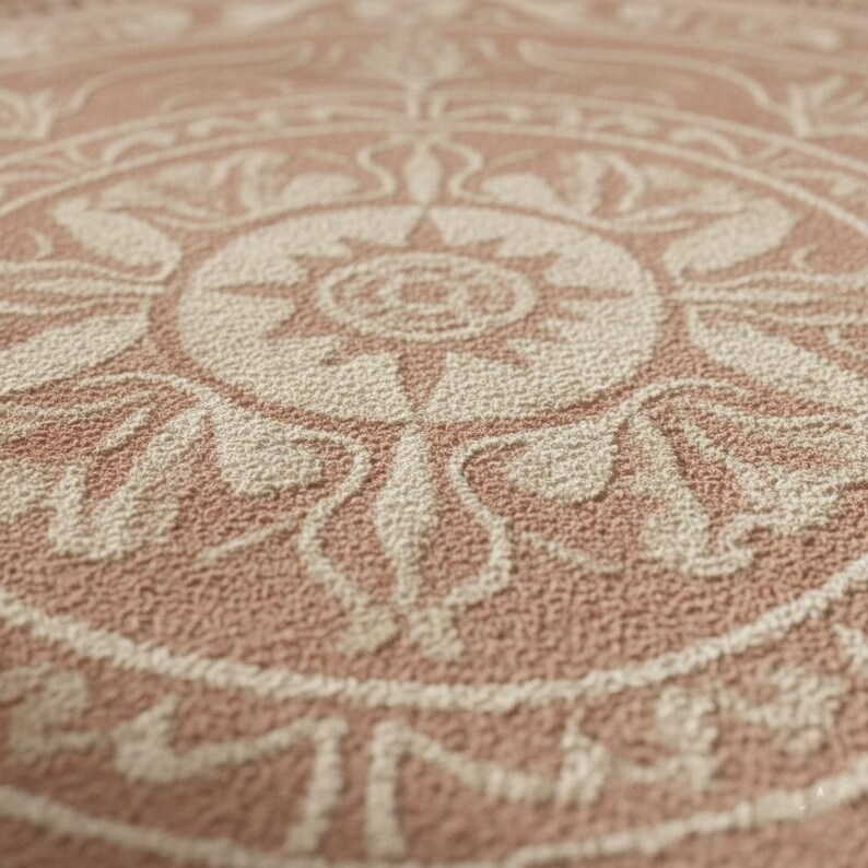 May include: Close-up of a textured, circular rug with a detailed, symmetrical design. The rug features a repeating pattern in shades of beige and dusty rose, creating a vintage or bohemian aesthetic. The design includes floral and geometric elements.