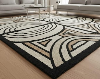 May include: A large area rug with a geometric design. The rug features a cream-colored background with black and tan abstract shapes. A thick black border frames the rug, which is placed on a hardwood floor.