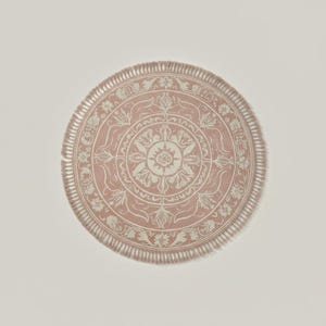May include: A round, pink rug with a detailed floral and geometric pattern in off-white. The rug has a fringed edge and a central medallion design. The rug is a decorative home accent.