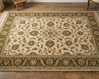 May include: A rectangular area rug featuring a cream-colored center field with an intricate olive green floral and vine pattern. The rug is framed by a wide olive green border with matching floral motifs and finished with cream-colored fringe.