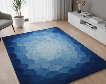 May include: A rectangular blue rug with a gradient pattern of overlapping, scalloped shapes. The rug transitions from a deep navy blue at the edges to a light blue center. The rug is placed on a light-colored wooden floor.