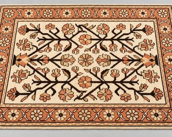 May include: A rectangular area rug featuring a cream-colored center with a symmetrical pattern of dark brown branches and peach-colored flowers. The rug is framed by a wide border in peach and cream with a repeating floral motif and fringed edges.