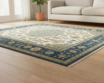 May include: A rectangular area rug with a cream-colored center and a navy blue border. The rug features a floral pattern in shades of blue, green, and tan. The rug is placed on a hardwood floor in a living room setting.