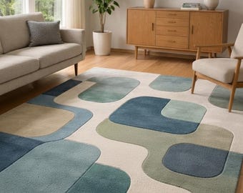 May include: A modern area rug with an abstract design. The rug features a cream-colored background with large, overlapping shapes in shades of blue, green, and tan. The rug is placed on a hardwood floor in a living room setting.