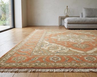 May include: An orange and beige patterned area rug with a fringed edge. The rug features a central medallion design and a detailed border. It is placed on a hardwood floor in a living room setting.