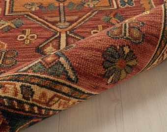 May include: Rolled-up area rug with a detailed, geometric pattern. The rug features a warm color palette of rust, orange, and beige, with accents of blue and green. The design includes floral and geometric motifs, creating a traditional aesthetic.