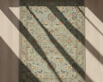 May include: A rectangular area rug with an intricate floral pattern in shades of teal, beige, and brown. The rug features a central medallion design and a detailed border. The rug is placed on a light-colored wooden floor, with sunlight casting shadows.