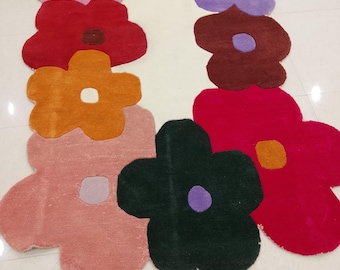 May include: A rectangular area rug featuring a border of large, multi-colored flower shapes in shades of pink, teal, purple, red, orange, dark green, and magenta, each with a contrasting center, surrounding a plain white center.