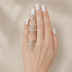 Puede incluir: Un anillo plateado que cubre todo el dedo, con un diseño de alambre continuo que se envuelve alrededor del dedo en una serie de bucles y curvas interconectadas, extendiéndose desde la base hasta justo debajo de la uña.