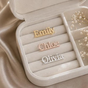 May include: Three custom name pins displayed inside a cream-coloured jewellery box. The top pin is gold-toned with the name Emily, the middle pin is rose gold-toned with the name Chloe, and the bottom pin is silver-toned with the name Olivia.