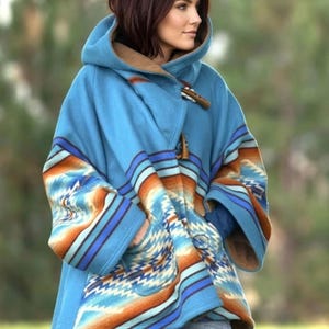 May include: A hooded coat in bright blue featuring a tan interior lining and a geometric pattern in shades of orange, white, and dark blue. The garment includes toggle closures and wide sleeves, worn over blue denim jeans with a visible pocket.
