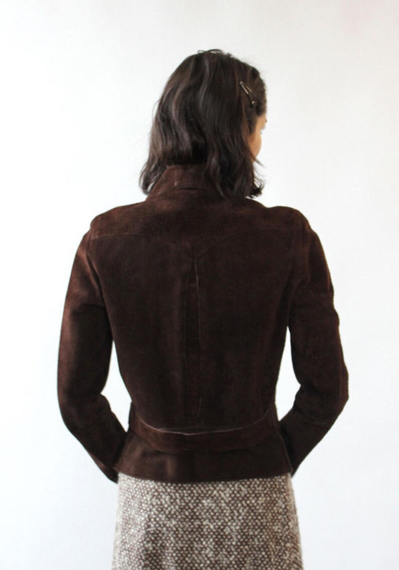 May include: A dark brown suede jacket with a high collar and a belt detail at the waist. The jacket has long sleeves and a tailored fit, showcasing a classic and elegant design. The back view highlights the jacket's structured silhouette.