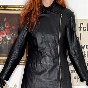 May include: Black leather jacket with an asymmetrical zip. The jacket features a notched collar and long sleeves. The jacket is a mid-length style.