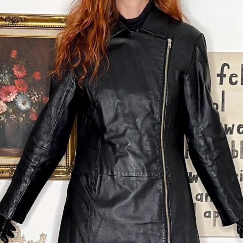 May include: Black leather jacket with an asymmetrical zip. The jacket features a notched collar and long sleeves. The jacket is a mid-length style.