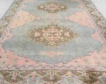 May include: A large rectangular area rug featuring a central medallion design in muted olive green and soft pink on a light blue background. The rug has a wide decorative border with repeating floral and geometric patterns in matching colors.