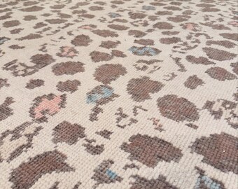 May include: A rectangular area rug featuring a cream-colored base with a repeating animal print pattern. The design consists of brown, soft pink, and light blue spots distributed across the surface, creating a textured appearance on the woven fabric.
