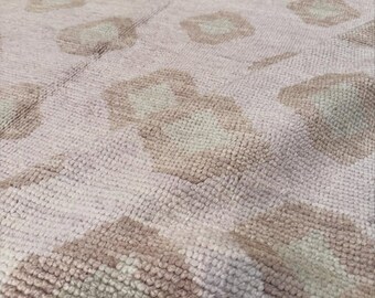 May include: A woven area rug featuring a repeating pattern of soft beige and light cream diamond shapes. The textile has a thick, textured pile with a visible knotted construction, creating a subtle depth across the surface of the floor covering.