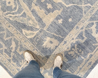 May include: A large area rug featuring a blue and cream-colored abstract pattern with geometric shapes and intricate motifs. The rug has a textured surface and is displayed from a top-down perspective, showing a repeating design across the fabric.