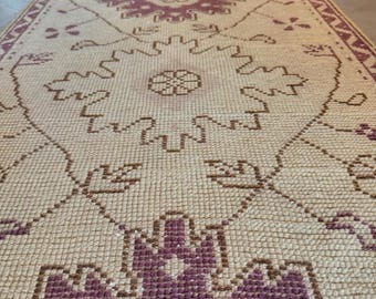 May include: A long, narrow runner rug featuring a cream-colored base with repeating geometric floral patterns in deep purple. The design includes intricate, symmetrical motifs arranged in a line, finished with a decorative purple border pattern.