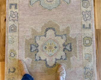 May include: A long, rectangular runner rug featuring a soft pink background with two large, symmetrical geometric medallions in shades of muted blue, beige, and sage green. The rug has a decorative border with repeating small geometric motifs.