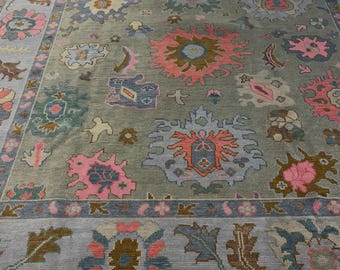 Peut inclure: Un grand tapis avec un fond vert sauge orné d'un motif répétitif de fleurs et de formes géométriques stylisées dans des tons rose, bleu clair, marron et crème. Le tapis présente une large bordure à motif floral et un bord uni.