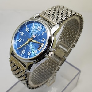 May include: A silver Seiko wristwatch with a blue patterned face and a silver strap. The watch face features white numerals and hands. The watch has a date display at the 3 o'clock position.