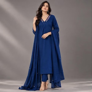 May include: A deep blue long-sleeved kurta dress featuring a V-neckline with delicate floral embroidery and small bead accents. The outfit includes matching trousers and a long, flowing blue dupatta draped over the shoulders and arms.