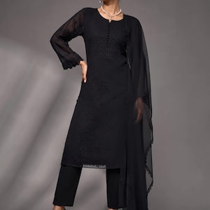 Puede incluir: Una t&uacute;nica negra de manga larga con intrincados bordados en tono sobre tono, una tapeta de botones en el escote y pu&ntilde;os festoneados. El conjunto incluye pantalones negros a juego y una dupatta negra transparente y ligera con borde festoneado.