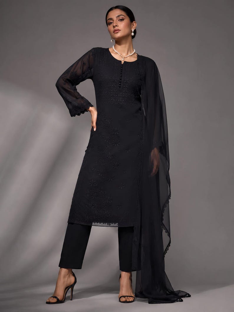Puede incluir: Una t&uacute;nica negra de manga larga con intrincados bordados en tono sobre tono, una tapeta de botones en el escote y pu&ntilde;os festoneados. El conjunto incluye pantalones negros a juego y una dupatta negra transparente y ligera con borde festoneado.