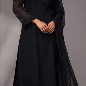 Puede incluir: Una t&uacute;nica negra de manga larga con bordados tonales intrincados, cuello redondo con tapeta de botones y pantalones rectos a juego. Un dupatta negro transparente con un borde de encaje festoneado completa el conjunto.