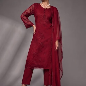 Puede incluir: Una t&uacute;nica de color granate de manga larga con intrincados bordados tonales y escote abotonado, combinada con pantalones rectos a juego y un dupatta ligero y transparente con un borde de encaje festoneado, usada con sandalias negras de tac&oacute;n.